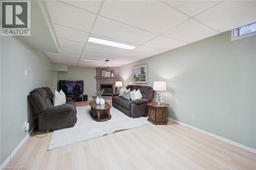 Neutral-toned room featuring a corner fireplace with stone surround, recessed drop ceiling, light-toned wood-finish flooring, and a single egress window - 11 Caledon Court, Cambridge, ON 