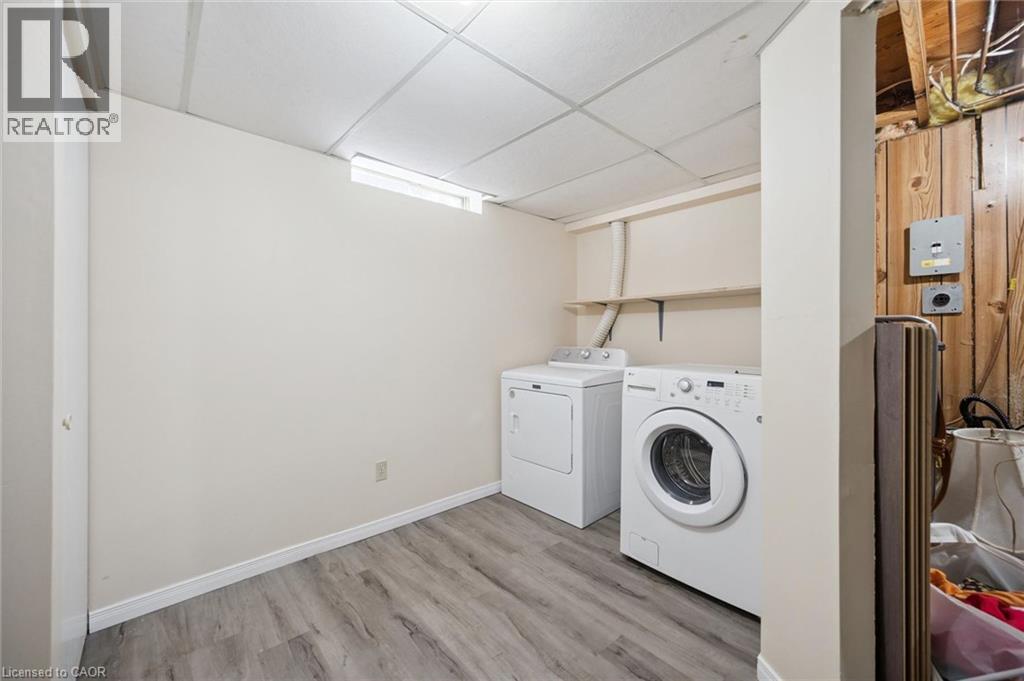 Laundry space featuring wood-finish flooring, a drop ceiling, a built-in wall shelf, and a rectangular hopper window - 11 Caledon Court, Cambridge, ON