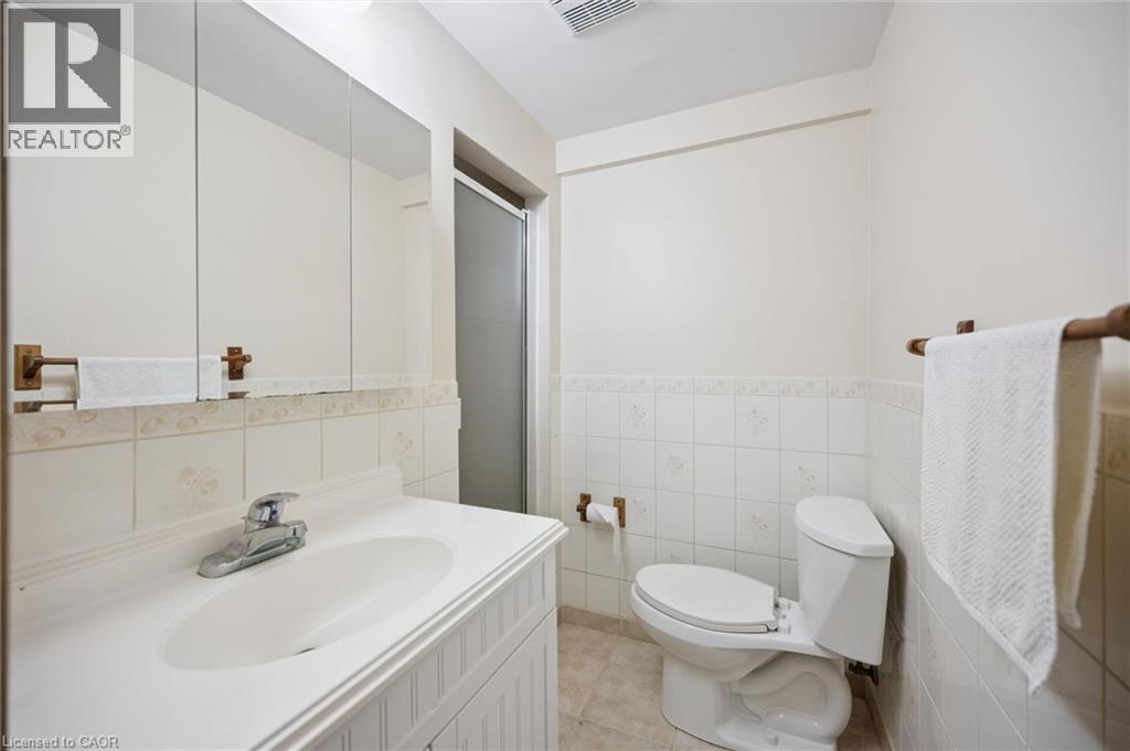 Bathroom featuring a white vanity with an integrated sink, large wall-mounted mirror, ceramic tile wainscoting, and a tiled shower enclosure - 11 Caledon Court, Cambridge, ON