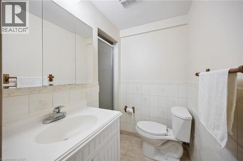 Bathroom featuring a white vanity with an integrated sink, large wall-mounted mirror, ceramic tile wainscoting, and a tiled shower enclosure - 11 Caledon Court, Cambridge, ON 