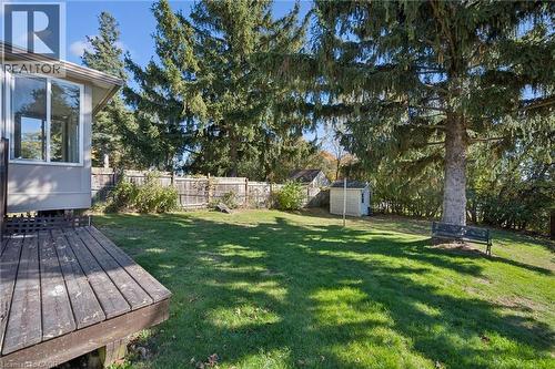 Private backyard featuring a wood deck, expansive lawn area, mature evergreen trees, and perimeter wood fencing - 11 Caledon Court, Cambridge, ON 