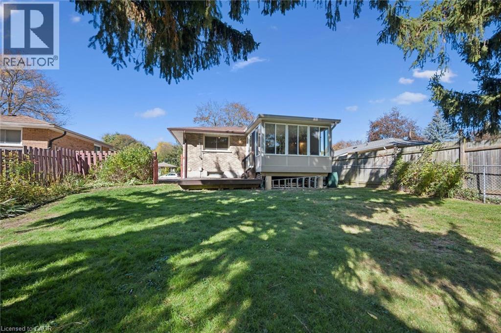 Expansive backyard featuring a grass lawn, enclosed sunroom with large windows, attached wooden deck, and perimeter wood fencing - 11 Caledon Court, Cambridge, ON