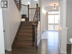 Staircase featuring wood treads, a wood handrail, and wrought-iron balusters, accompanied by wood-finish flooring, a decorative column, and glass sliding doors -