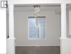 Architectural columns featuring square pedestal bases, central window with neutral trim, wood-finish flooring, and a tiered crystal chandelier -