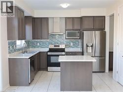Kitchen featuring charcoal-toned cabinetry, stainless steel appliances, a mosaic tile backsplash, stone-composite countertops, and a central island -