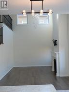 High-ceiling interior featuring wood-finish flooring, a linear four-light chandelier, a fireplace with a white mantel, and black metal stair railings -