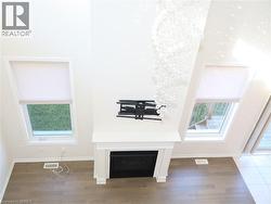 Double-height living area featuring a central fireplace with white mantle, wood-finish flooring, two large windows with cellular shades, and a multi-tiered crystal chandelier -