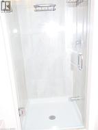 Shower stall featuring a glass door, polished chrome hardware, light-toned wall tile, and a built-in caddy -