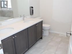 Dual-sink vanity with dark wood-finish cabinetry, solid surface countertop, large wall-mounted mirror, and tile flooring -