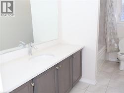 Bathroom featuring a dark-finish vanity with a light-toned countertop, undermount sink, chrome faucet, wall-spanning mirror, and tile flooring -