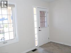 White door with upper glass panel, full-length sidelight, multi-pane window with custom trim, and neutral carpeting -