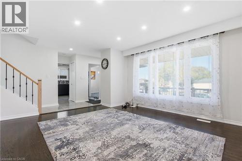 Open-concept area featuring dark-tone wood-finish flooring, recessed lighting, a large picture window, and a staircase with a natural wood handrail and black metal balusters - 90 June Street, Hamilton, ON 