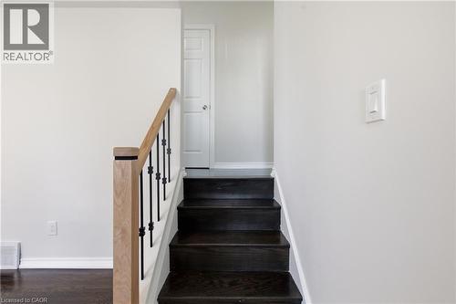 Staircase featuring dark wood-finish treads, a light wood-finish newel post and handrail, and black metal balusters - 90 June Street, Hamilton, ON 