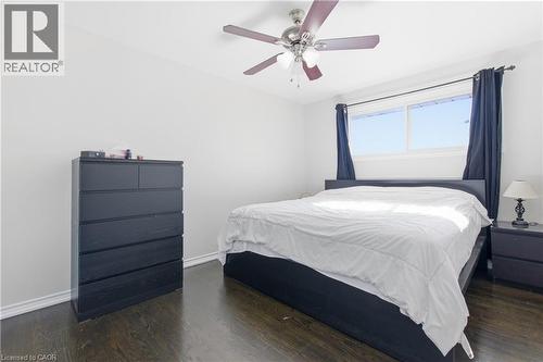 Room featuring dark-stained wood-finish flooring, a ceiling fan with integrated lighting, and a large horizontal window - 90 June Street, Hamilton, ON 