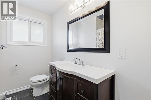 Dark wood-finish vanity with an integrated white sink, framed wall mirror, three-light vanity fixture, and tiled flooring - 90 June Street, Hamilton, ON 