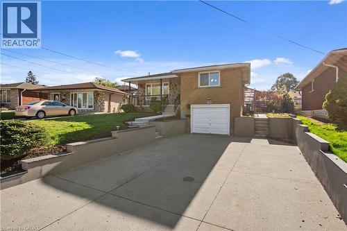 Split-level exterior featuring a brick and stone facade, integrated single-car garage, concrete driveway, and tiered retaining walls - 90 June Street, Hamilton, ON 