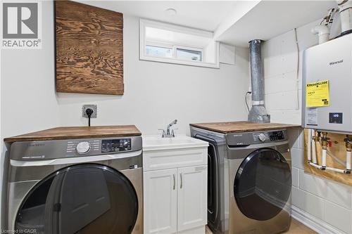 Laundry area featuring a utility sink with a white cabinet base, wall-mounted tankless water heater, and custom wood-finish folding countertops - 90 June Street, Hamilton, ON 