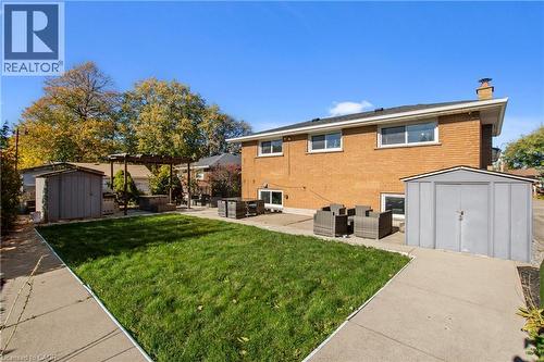 Brick exterior featuring a concrete patio, wood-frame pergola, lawn space, and two detached storage structures - 90 June Street, Hamilton, ON 
