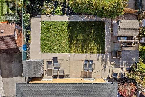 Backyard featuring a central grass lawn, wraparound concrete patio, and two detached storage structures - 90 June Street, Hamilton, ON 