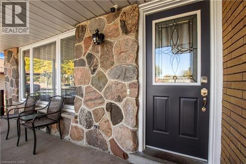 Front entrance featuring natural stone cladding, a dark-finished entry door with an ornate leaded glass insert, and exterior sconce lighting - 90 June Street, Hamilton, ON 