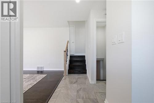 Interior foyer featuring large-format neutral tile flooring, dark-stained wood stair treads, and a wooden handrail with metal balusters - 90 June Street, Hamilton, ON 