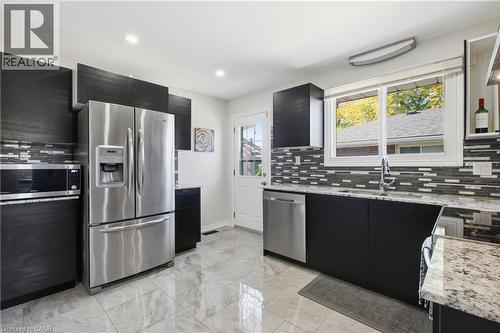 Kitchen featuring dark cabinetry, stone-finish countertops, stainless steel appliances, a multi-tone tile backsplash, and polished tile flooring - 90 June Street, Hamilton, ON 