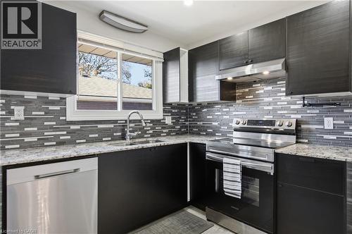 Kitchen featuring dark cabinetry, stone-finish countertops, linear tile backsplash, and stainless steel appliances - 90 June Street, Hamilton, ON 