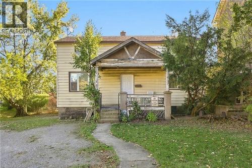 Two-story home with horizontal siding, a covered front porch featuring a gabled roofline, concrete foundation, and an gravel driveway - 14 London Street N, Hamilton, ON 