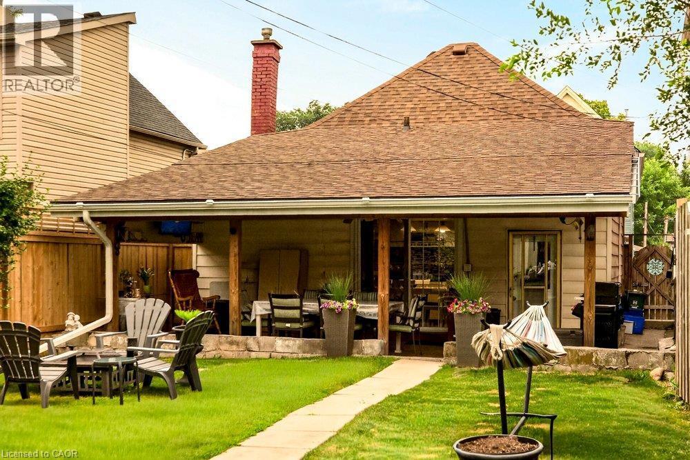 Expansive rear yard featuring a covered porch, established lawn, and stone retaining wall - 66 Beechwood Avenue, Hamilton, ON