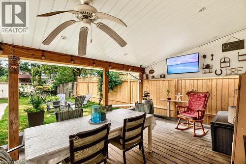 Covered outdoor patio with wood decking and ceiling, featuring an outdoor dining area with mounted TV and ceiling fan - 66 Beechwood Avenue, Hamilton, ON 