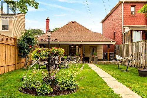 Expansive rear yard featuring a manicured lawn, established garden beds, and a paved pathway leading to the covered porch - 66 Beechwood Avenue, Hamilton, ON 