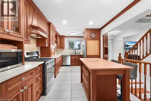 Kitchen featuring wood-finish cabinetry, stainless steel appliances, light-toned countertops, and a center island with seating - 31 Berrisfield Crescent, Hamilton, ON 