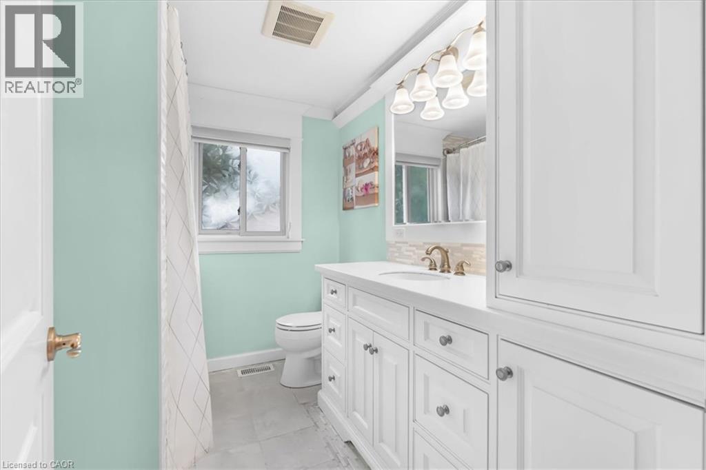 White vanity with a single basin sink, brass-finish faucet, and a wall-mounted light fixture - 31 Berrisfield Crescent, Hamilton, ON