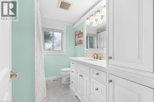 White vanity with a single basin sink, brass-finish faucet, and a wall-mounted light fixture - 31 Berrisfield Crescent, Hamilton, ON 