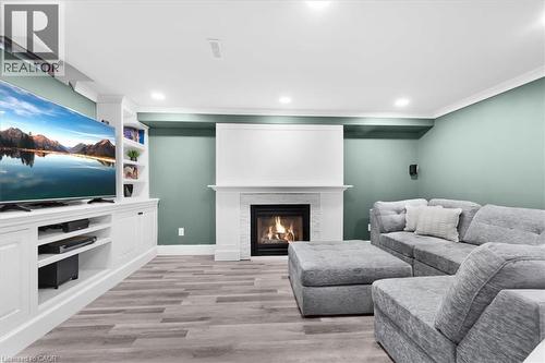 Built-in media console with open shelving, recessed lighting, wood-finish flooring, and a fireplace with a stone surround and white mantel - 31 Berrisfield Crescent, Hamilton, ON 