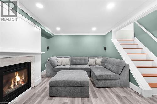 Recessed lighting, wood-finish flooring, white trim, staircase with wood treads, and a built-in fireplace with a stone surround - 31 Berrisfield Crescent, Hamilton, ON 