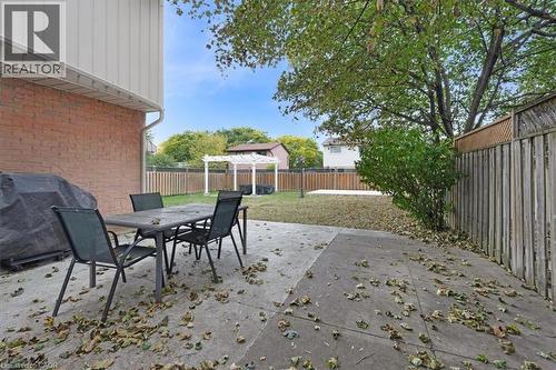 Concrete patio with brick exterior, featuring a wood fence, mature trees, and a white pergola structure - 31 Berrisfield Crescent, Hamilton, ON 