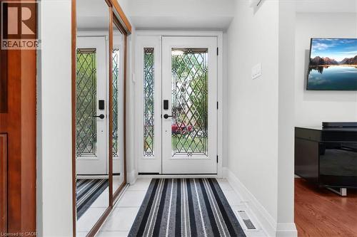 Double front doors with decorative glass panels, sidelight window, white tile flooring, and wood-finish accent wall - 31 Berrisfield Crescent, Hamilton, ON 