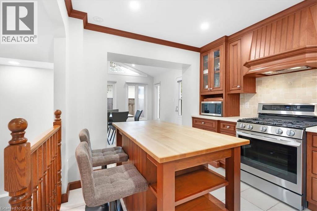 Hardwood kitchen island with butcher block countertop, stainless steel range, built-in microwave, and wood cabinetry with glass-front accents - 31 Berrisfield Crescent, Hamilton, ON