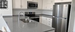 Kitchen featuring light-finish cabinetry, gray stone-composite countertops, stainless steel appliances, and a double-basin undermount sink with a high-arch faucet - 