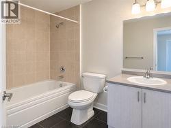 Bathroom featuring a neutral-toned tile shower surround, bathtub with chrome fixtures, vanity with a stone-finish countertop, undermount sink, and dark tiled flooring - 