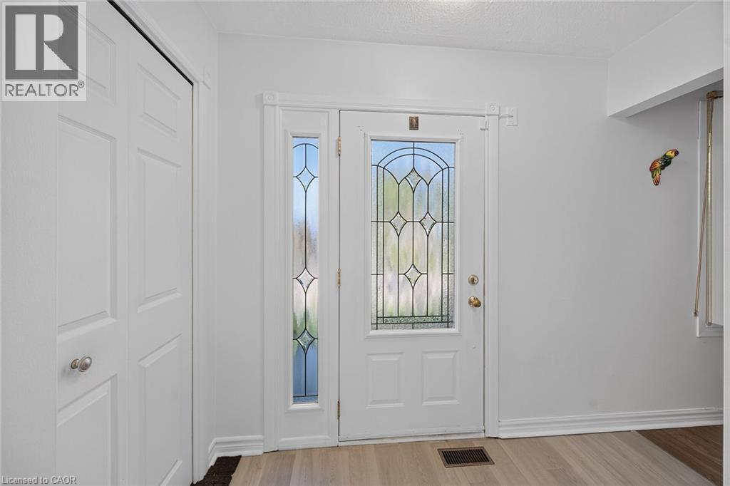 Entryway featuring a solid door with decorative leaded glass inserts, a matching full-length sidelight, wood-finish flooring, and a multi-panel closet door - 411 Queen Victoria Drive, Hamilton, ON