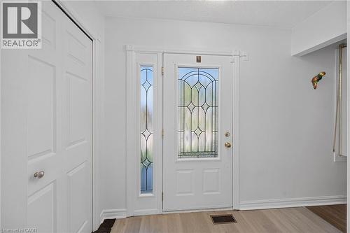 Entryway featuring a solid door with decorative leaded glass inserts, a matching full-length sidelight, wood-finish flooring, and a multi-panel closet door - 411 Queen Victoria Drive, Hamilton, ON 