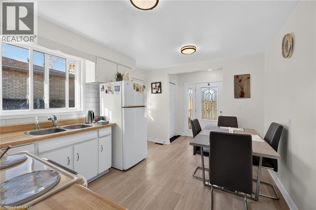 Kitchen featuring wood-finish flooring, wood-toned countertops, white cabinetry, a dual-basin stainless steel sink, and a decorative glass-panel exterior door - 411 Queen Victoria Drive, Hamilton, ON