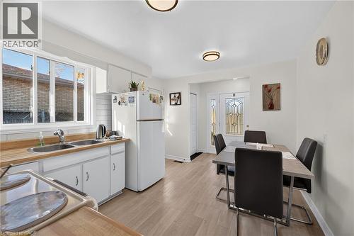Kitchen featuring wood-finish flooring, wood-toned countertops, white cabinetry, a dual-basin stainless steel sink, and a decorative glass-panel exterior door - 411 Queen Victoria Drive, Hamilton, ON 