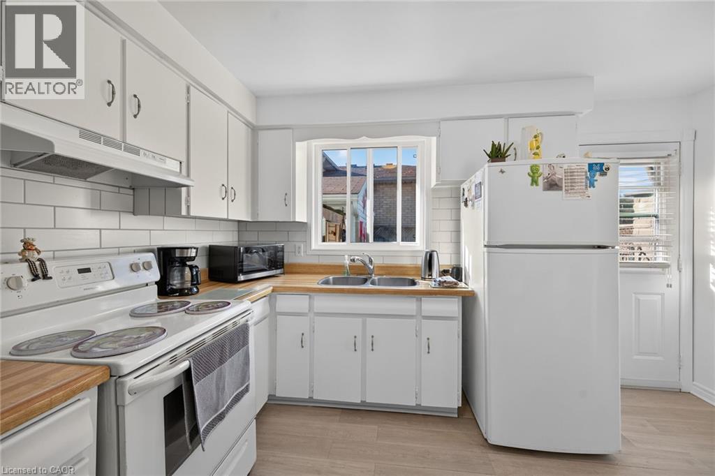 Kitchen featuring white cabinetry, wood-finish countertops, subway tile backsplash, dual-basin sink, and wood-finish flooring - 411 Queen Victoria Drive, Hamilton, ON