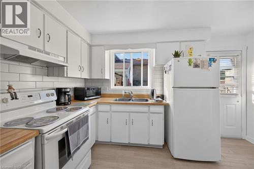 Kitchen featuring white cabinetry, wood-finish countertops, subway tile backsplash, dual-basin sink, and wood-finish flooring - 411 Queen Victoria Drive, Hamilton, ON 