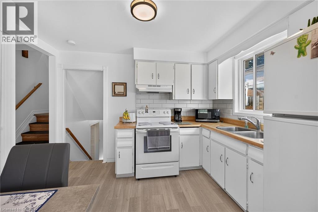 Kitchen featuring white cabinetry, wood-finish countertops, subway tile backsplash, stainless steel double-basin sink, and wood-finish flooring - 411 Queen Victoria Drive, Hamilton, ON