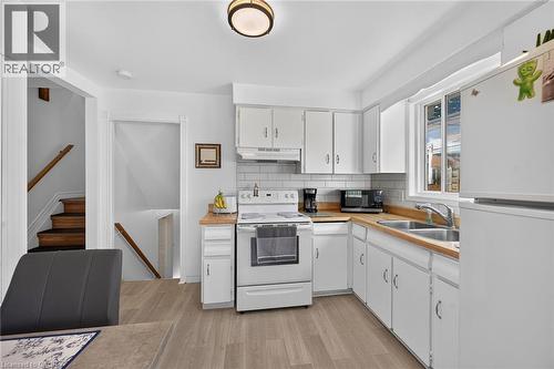 Kitchen featuring white cabinetry, wood-finish countertops, subway tile backsplash, stainless steel double-basin sink, and wood-finish flooring - 411 Queen Victoria Drive, Hamilton, ON 