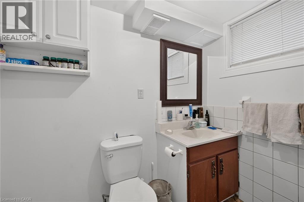 Bathroom featuring white cabinetry, integrated sink, wooden vanity base, framed mirror, and white wall-tiled surround - 411 Queen Victoria Drive, Hamilton, ON